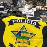 Equipamentos eletrônicos, tabletes de maconha, pinos de cocaína e um drone profissional dispostos sobre uma mesa de delegacia como material apreendido.