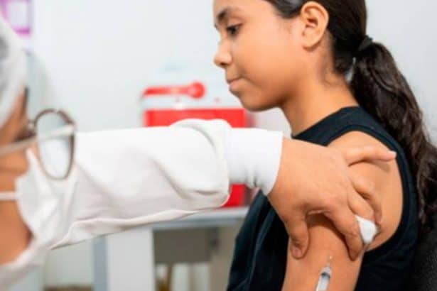 Cartão de vacinação do SUS sobre uma mesa de consultório médico, com um frasco de vacina ao fundo.