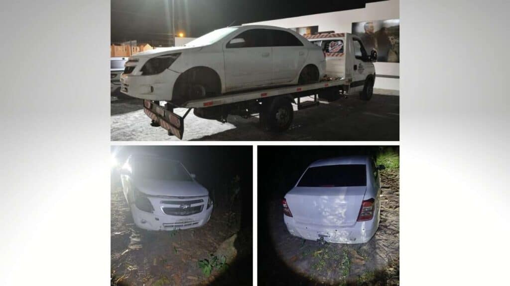 Parte dianteira de um automóvel Chevrolet Cobalt de cor branca abandonado em uma área de vegetação densa no interior do estado.