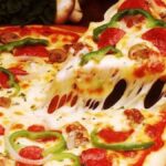 Mãos de pizzaiolo preparando massa de pizza de trigo em ambiente profissional.