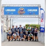 Atletas da equipe Lagartos Race Team reunidos no pódio, segurando troféus e medalhas de ouro, vestindo o uniforme oficial de ciclismo.