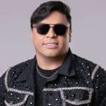 Foto de estúdio do cantor Neto Araújo sorrindo e segurando um microfone durante uma apresentação musical de forró.