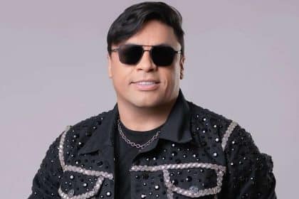 Foto de estúdio do cantor Neto Araújo sorrindo e segurando um microfone durante uma apresentação musical de forró.