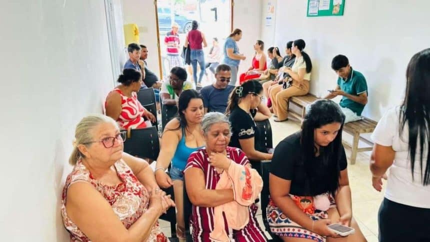 Moradores do povoado Itaperinha em fila organizada aguardando atendimento médico dentro de uma estrutura móvel de saúde da prefeitura.