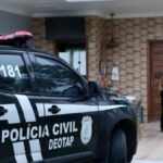 Cinco policiais civis de Sergipe em pé ao lado de uma viatura preta estacionada em rua residencial durante o início da manhã.