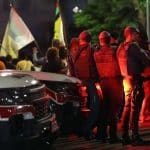 Movimentação de viaturas policiais e peritos em uma comunidade urbana durante a noite, com foco em luzes de emergência.