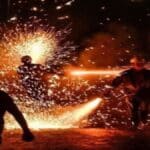 Centelhas e fumaça geradas pela queima de fogos tradicionais em uma rua de paralelepípedos durante festividade junina noturna em Sergipe.